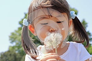 Japanese girl blowing dandelion seeds under the blue sky