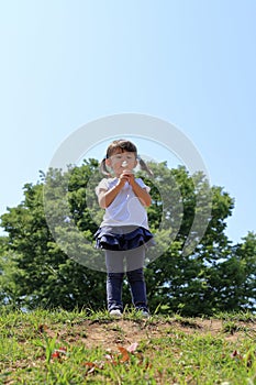 Japanese girl blowing dandelion seeds under the blue sky