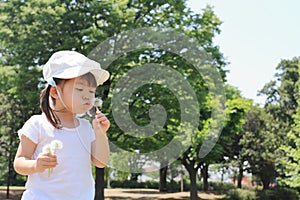Japanese girl blowing dandelion seeds under the blue sky