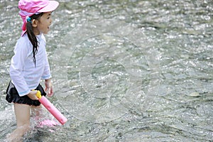 Japanese girl playing in the river with water gun