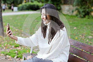 Japanese girl sitting on bench and making video call by smartphone.