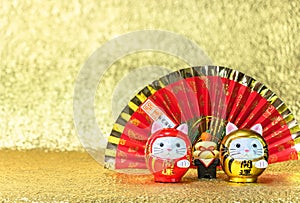 Japanese greeting card depicting a red handheld fan and two cat daruma figurines on a gold background.