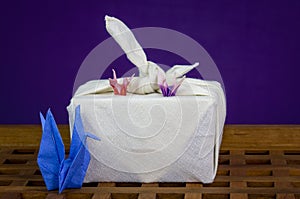 Japanese handmade origami swans with Furoshiki fabric wrapped gift, on wooden tray