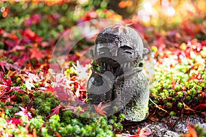 Japanese Jizo sculpture doll with falling Red Maple leaf in Japanese Garden at Enkoji Temple, Kyoto, Japan. Landmark and famous in