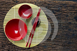 Japanese kitchenware set of red chopsticks, bowls and cup on bamboo mat and wooden table background