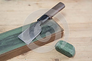 Japanese leather craft knife on a leather knife strop with green polishing compound on a wooden surface