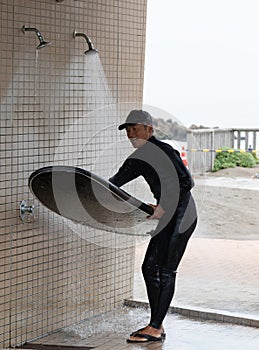 Japanese man in black wetsuit cleaning up his surfboard