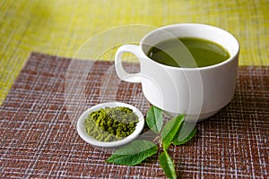 Japanese matcha green tea is poured into a white mug and on a white saucer in powder.