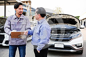 Japanese Mechanic show car checking list for Asian customer with an opened radiator hood car. Focus on mechanic and customer.