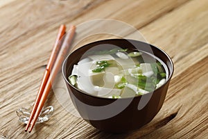 Japanese Miso Soup with Spring Onion and Cubed Tofu In a Brown Bowl, Wooden Table