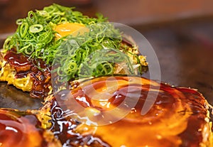 Japanese okonomiyaki omelet topped with fried egg and chopped scallions.