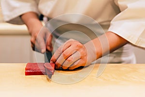 Japanese Omakase Chef cut bluefin tuna Otoro in Japanese neatly by knife on wooden kitchen counter for making sushi.