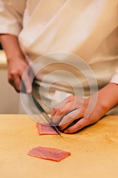 Japanese Omakase Chef cut Medium Fatty Bluefin Tuna Chutoro in Japanese neatly by knife on wooden kitchen counter.