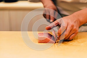 Japanese Omakase Chef cut Medium Fatty Bluefin Tuna Chutoro in Japanese neatly by knife on wooden kitchen counter.