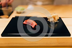 Japanese Omakase meal: Chutoro Bluefin Tuna Sushi served by hand with pickled ginger on glossy black plate. Japanese luxury meal
