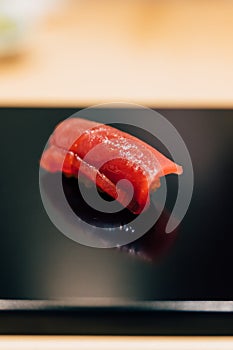 Japanese Omakase meal: Close up Chutoro Bluefin Tuna Sushi served by hand with pickled ginger on glossy black plate.