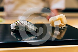 Japanese Omakase Menu: Saba Sushi Mackerel sprinkle minced Yuzu peel served by hand with pickled ginger on glossy black plate.