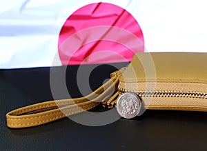 Japanese one hundred Yen coins on obverse Sakura blossoms with sand color wallet on black floor and Japan flag background