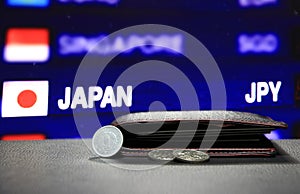 Japanese one Yen coins on reverse JPY and pile of other Japanese coins on black floor with black wallet and digital board.