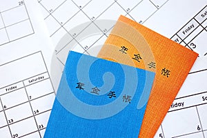 Japanese pension insurance booklets on table with calendar. Blue and orange pension book