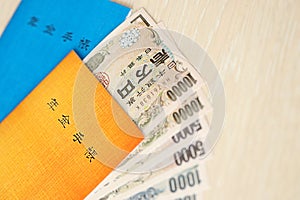 Japanese pension insurance booklets on table with yen money bills. Blue and orange books