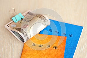 Japanese pension insurance booklets on table with yen money bills. Blue and orange books