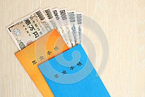 Japanese pension insurance booklets on table with yen money bills. Blue and orange books