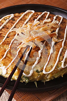 Japanese pizza: okonomiyaki on a plate and chopsticks. Vertical