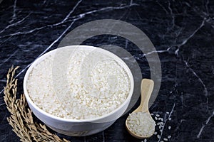 Japanese rice in white ceramic bowl and wooden spoon on dark marble table