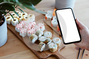 Japanese rolls and mobile phone in hand on a wooden backgroundJapanese rolls and mobile phone in hand on a wooden background