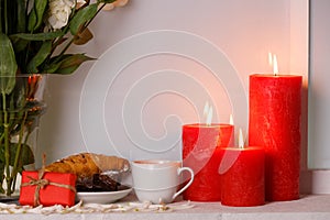 Japanese roses in a vase of water next to breakfast and burning candles close-up on a window-sill