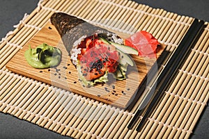 Japanese sashimi with salmon, rice, cucumber, lettuce and tobiko caviar with black sesame seeds. Food on a wooden stand on a
