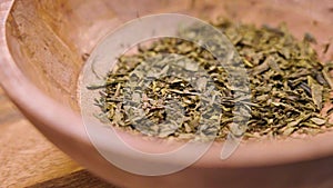 Japanese sencha dried tea leaves in rustic wooden bowl. Falling dried green ingredient