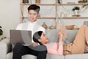 Japanese Spouses Relaxing With Laptop And Book In Living Room