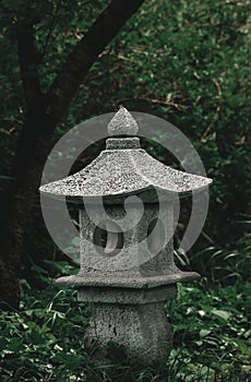 Japanese stone lantern in beautiful asian zen garden full of fresh green plants and flowers