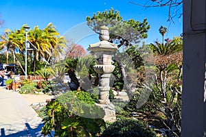 A Japanese stone tower in a garden surrounded by lush green plants and trees near a walking path