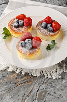 Japanese style sluffy souffle pancake dessert with blueberry and strawberry close-up on a plate. Vertical