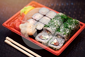 Japanese sushi in red plastic container for carrying food on black. Roll made of crab meat, avocado, cucumber inside and