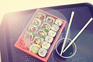 Japanese sushi in red plastic container for carrying food on black. Roll made of crab meat, avocado, cucumber inside and