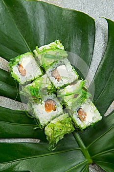 Japanese sushi roll with Chuka hiyashi wakame seaweed Chukka on tropical monstera leaf, stone background