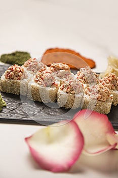 Japanese sushi roll with salmon served on plate, pink rose petals, heart shapes of spices on marble background