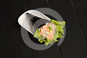 Japanese Sushi Sake Temaki with salmon, rice, Tobiko roe eggs, avocado and salad leaf in nori seaweed on white plate.