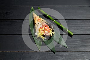 Japanese Sushi Temaki Hand Roll with salmon in Mamenori seaweed on bamboo leaves near bamboo plant stick
