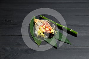 Japanese Sushi Temaki Hand Roll with salmon in Mamenori seaweed on bamboo leaves near bamboo plant stick