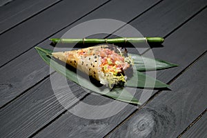 Japanese Sushi Temaki Hand Roll with salmon in Mamenori seaweed on bamboo leaves near bamboo plant stick