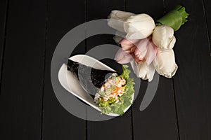 Japanese Sushi Temaki with tiger shrimp wrapped in nori seaweed served on white plate with pastel tulips on background