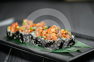 Japanese sushi volcano roll with black flying fish roe tobiko and Marinated salmon on top Served on bamboo leaves on black plate