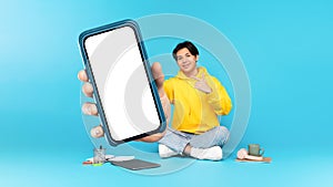 Japanese Teen Guy Showing Large Phone Sitting On Blue Background