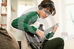 Japanese Teen Guy Wearing Headphones Learning Electric Guitar At Home