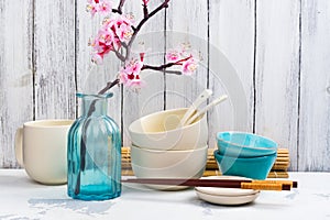 Japanese utensils, dinnerware, chopsticks and branch of blooming sakura on white asian background